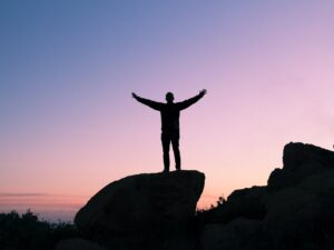 silhouette of person with outstretched arms on large rock against sunrise