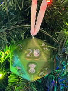 green D20 ornament with silver glitter numbers and silver ribbon hanging on tree