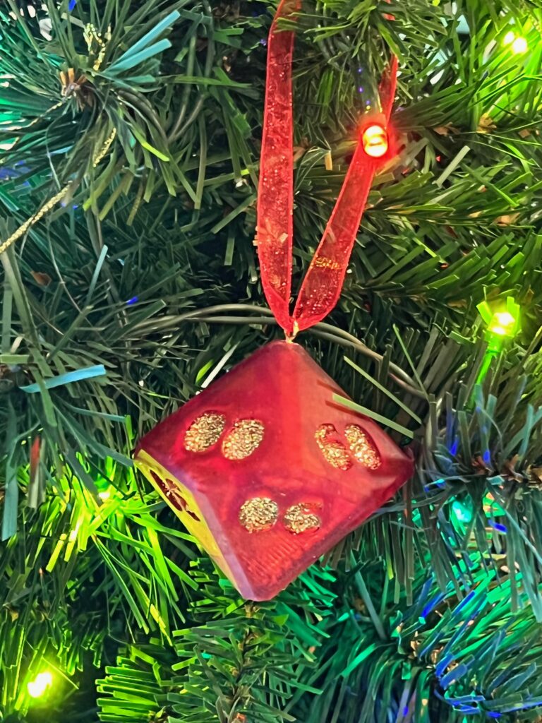 red D100 ornament with gold glitter numbers and red ribbon hanging on tree