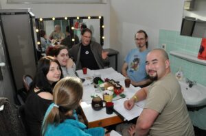 a variety of people sitting at a table playing a tabletop roleplaying game near a sink