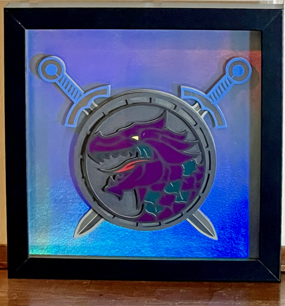 a picture of a purple & blue dragon head on a round shield with swords in a frame