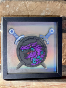 a picture of a purple & blue dragon head on a round shield with swords in a frame on a brick mantle