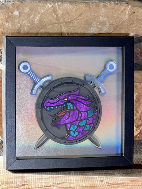 a picture of a purple & blue dragon head on a round shield with swords in a frame on a brick mantle