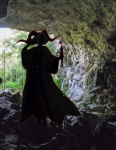 silhouette of a tiefling in a trenchcoat standing in the interior mouth of a cave