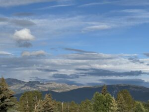 a mountain landscape with trees in the foreground and a blue cloudy sky