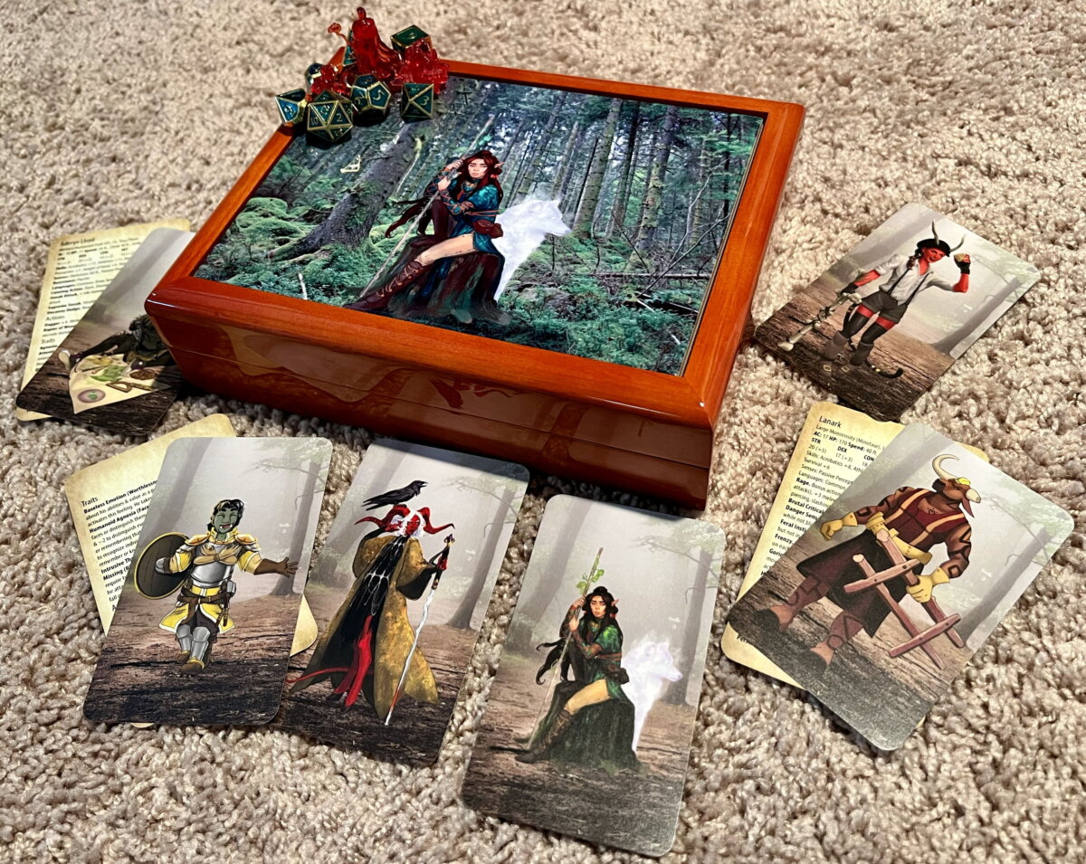wooden case with image of elf in woods on top, minis & dice on top, NPC cards on floor around it